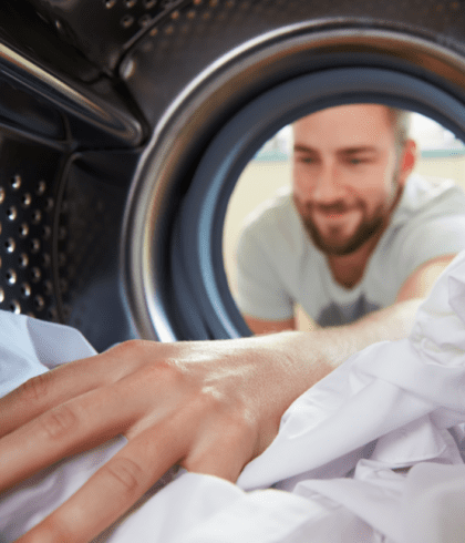 Close up image of a young adult male pulling laundry out of a dryer